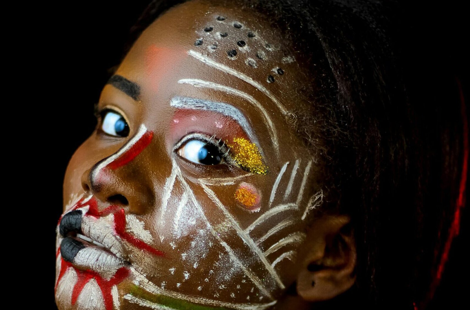 Close-up portrait of a woman with vivid body paint on a black background.