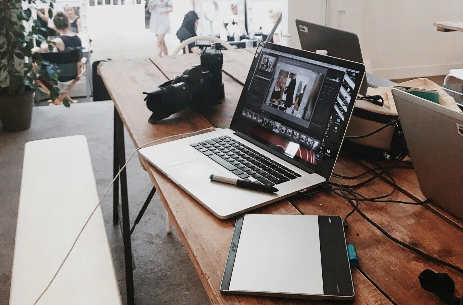 A bright, modern workspace featuring laptops, a camera, and a drawing tablet in an indoor office.